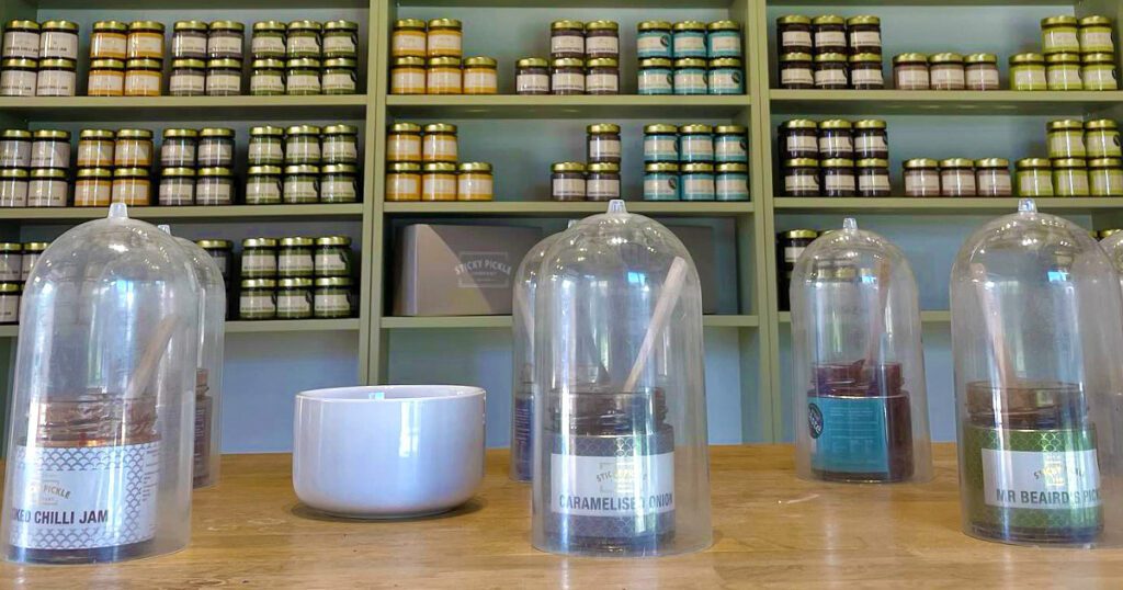 The tasting table at the Sticky Pickle Pantry with shelves of pickles and chutneys