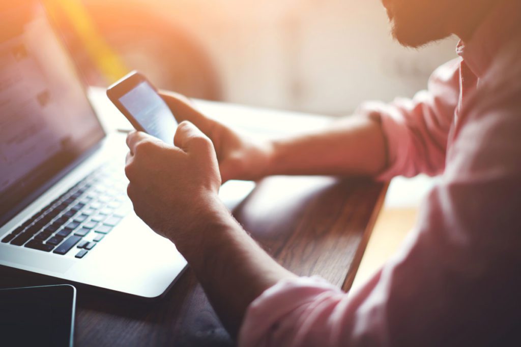 Man holding a smartphone and using a laptop image for why you should include digital assets in your will blog