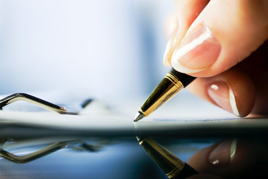 Close up of a woman's hand holding a pen and signing a document image for why business owners should make a will blog
